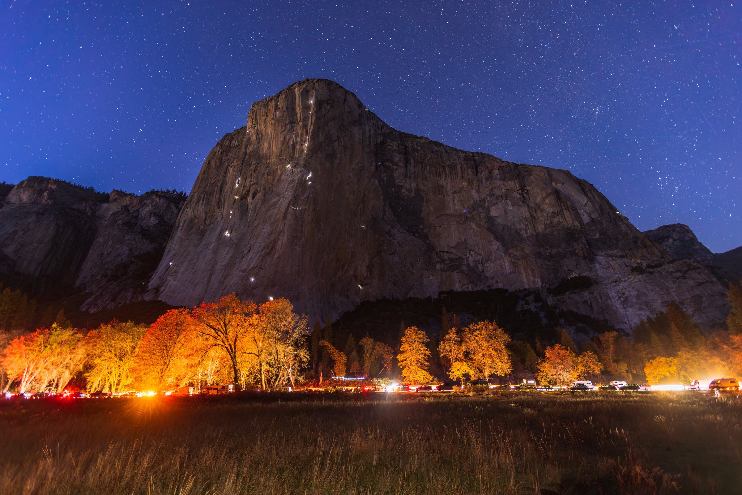 Long exposure of El Capitan at night under the stars in Yosemite, with tiny climber headlamps on the granite wall