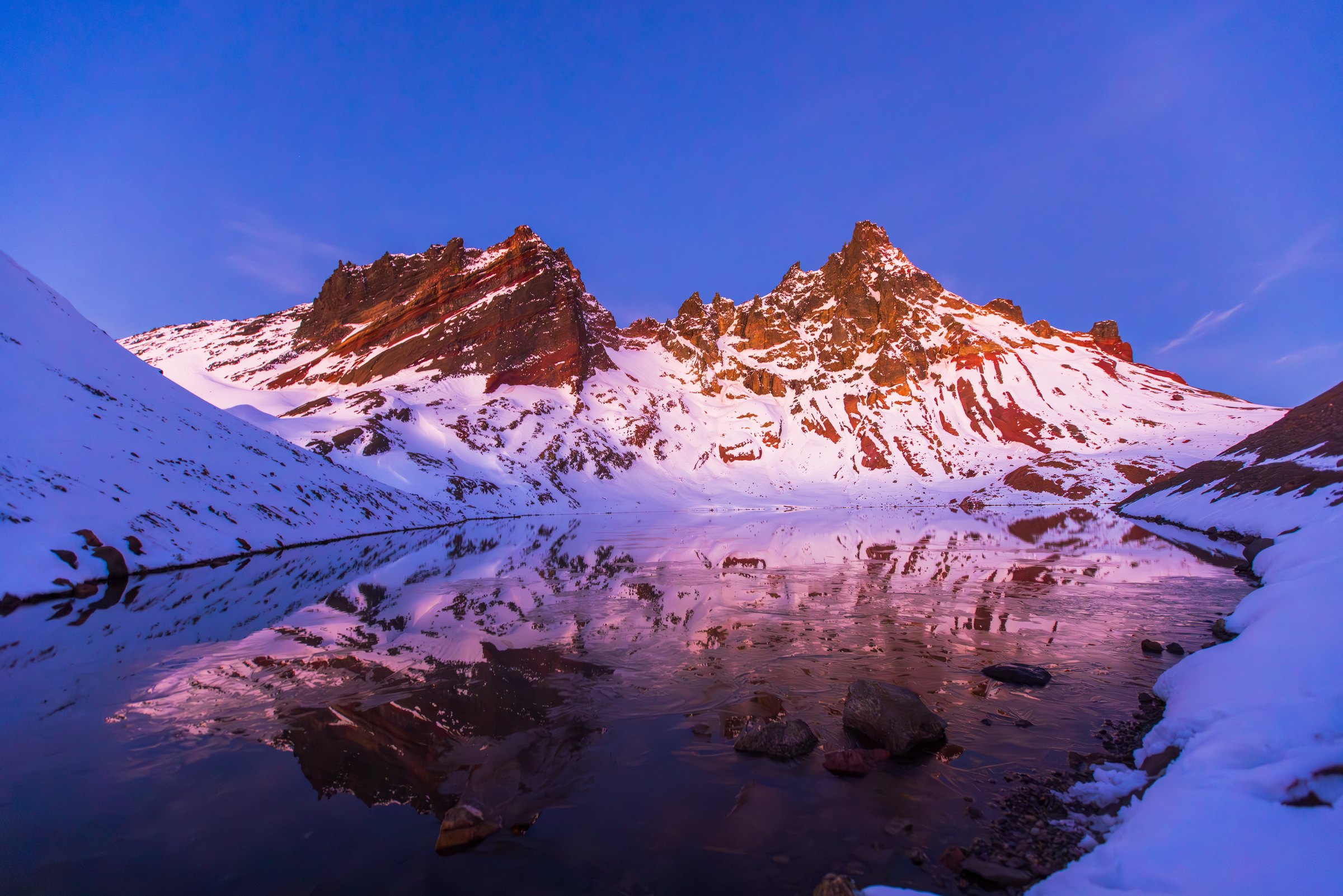 Snowy jagged peaks glowing pink at sunset, reflected in a still alpine lake near Bend, Oregon