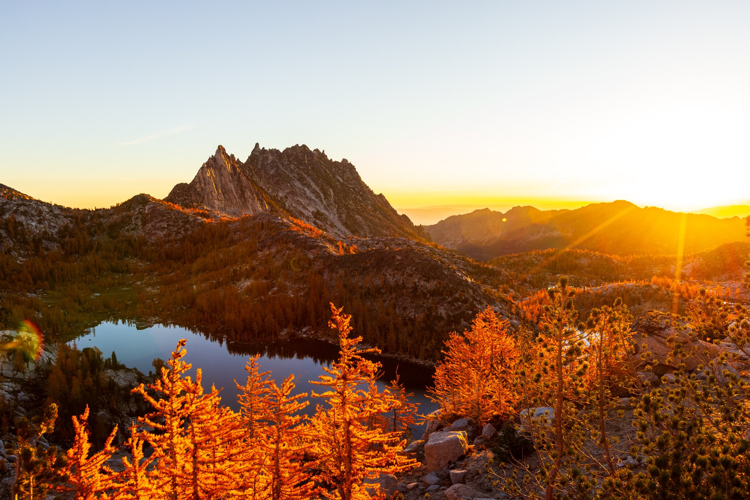 Sunrise over jagged peaks and an alpine lake ringed with golden larches in the Enchantments